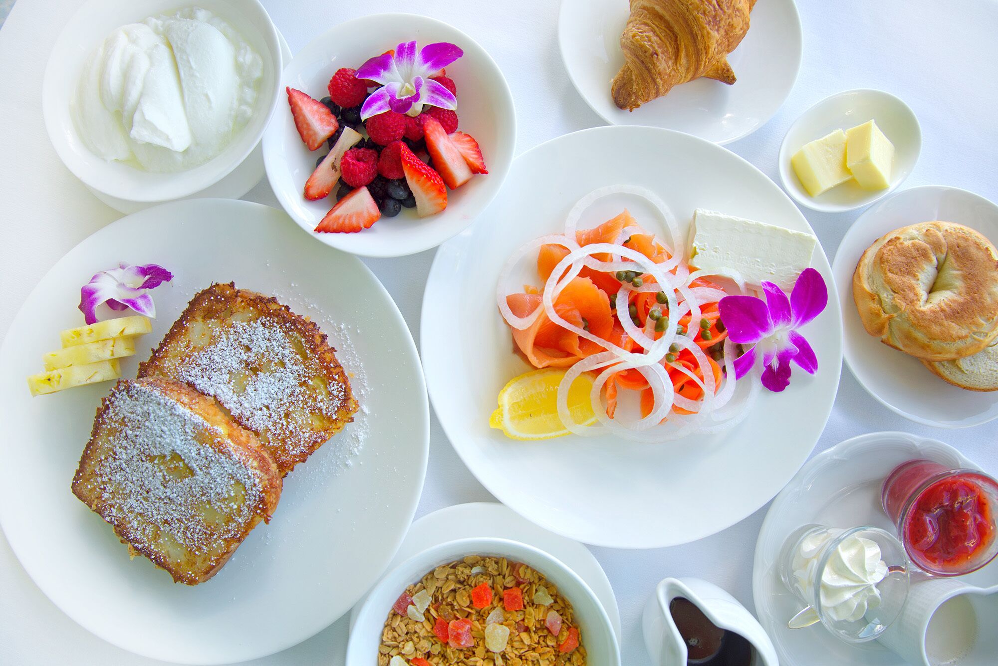Verschiedene Frühstücksleckereien wie Toast, Obstsalat, Räucherlachs und Gebäck auf einem Tisch.