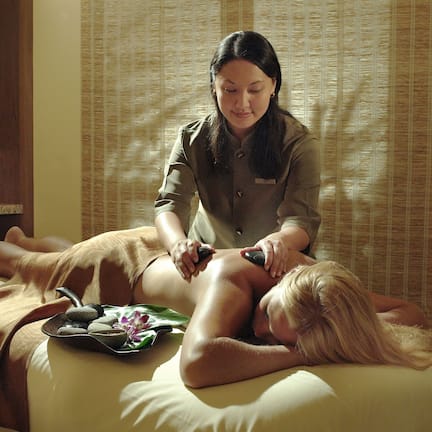 A massage therapy session in a room with a bed, a small table with candles, and a potted plant.