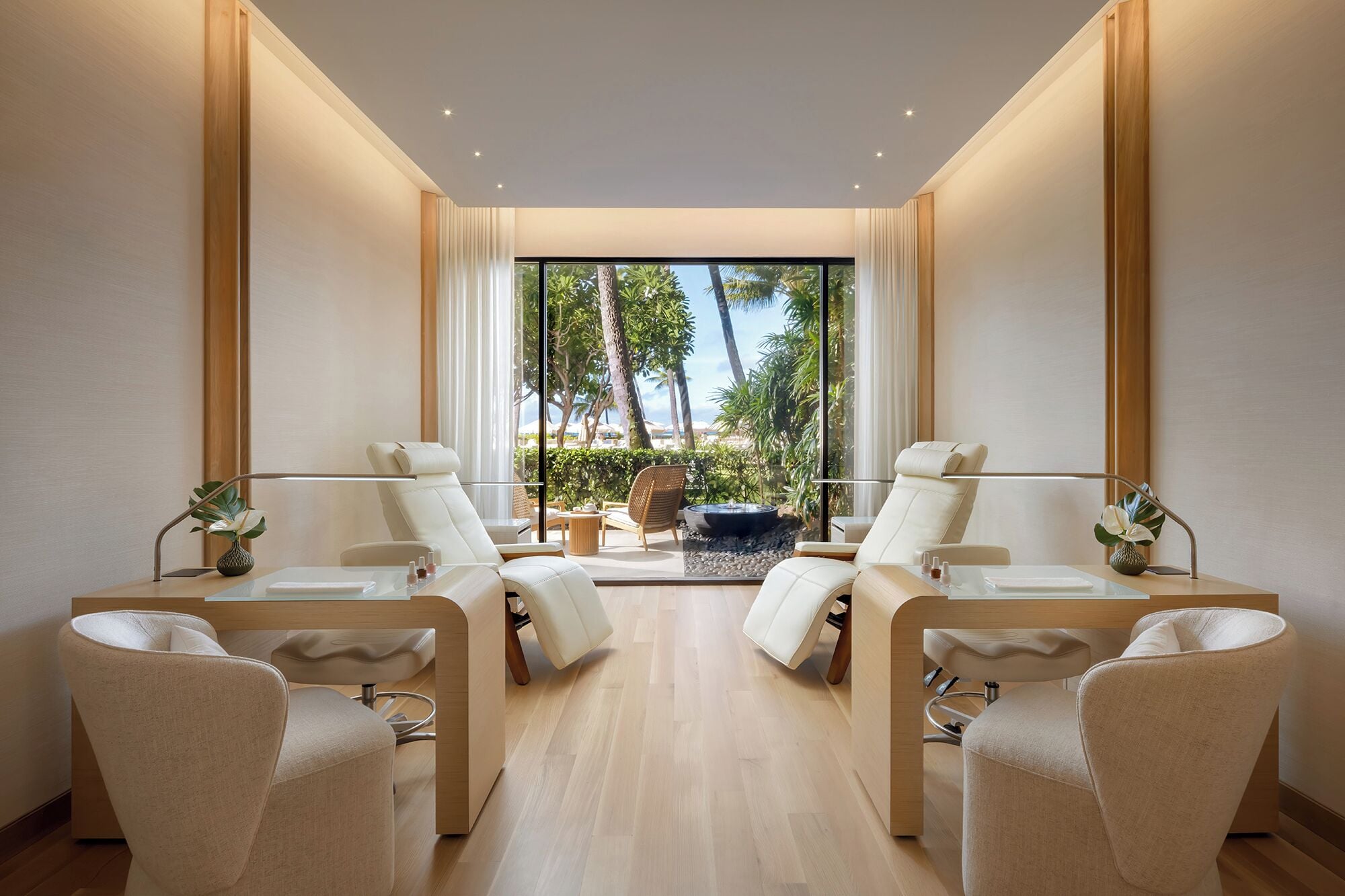 Un spa con dos sillones de masaje, una mesita con botellas, y vistas a palmeras y una piscina.