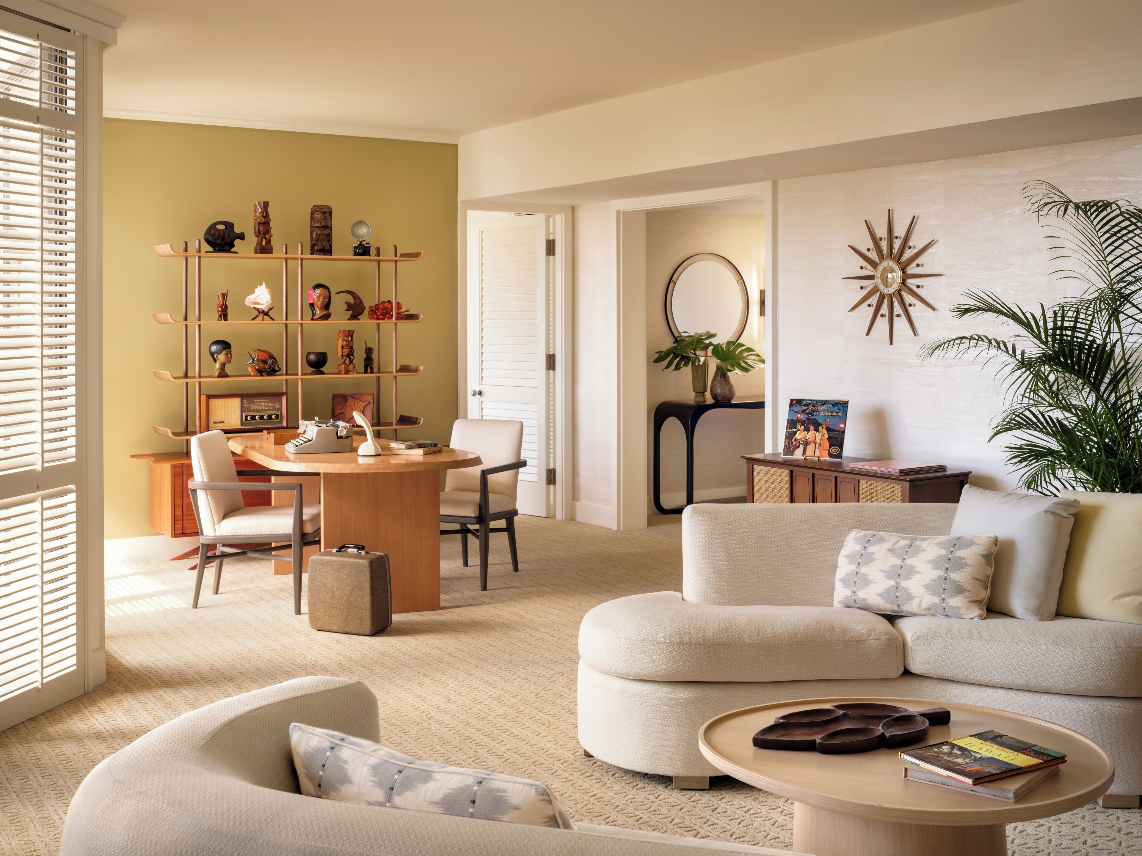 A modern living room with a round wooden table, a beige sofa, and a bookshelf filled with decorative items.
