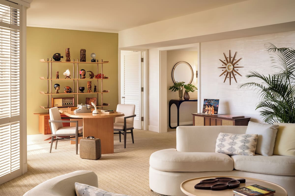 A modern living room with a round wooden table, a beige sofa, and a bookshelf filled with decorative items.