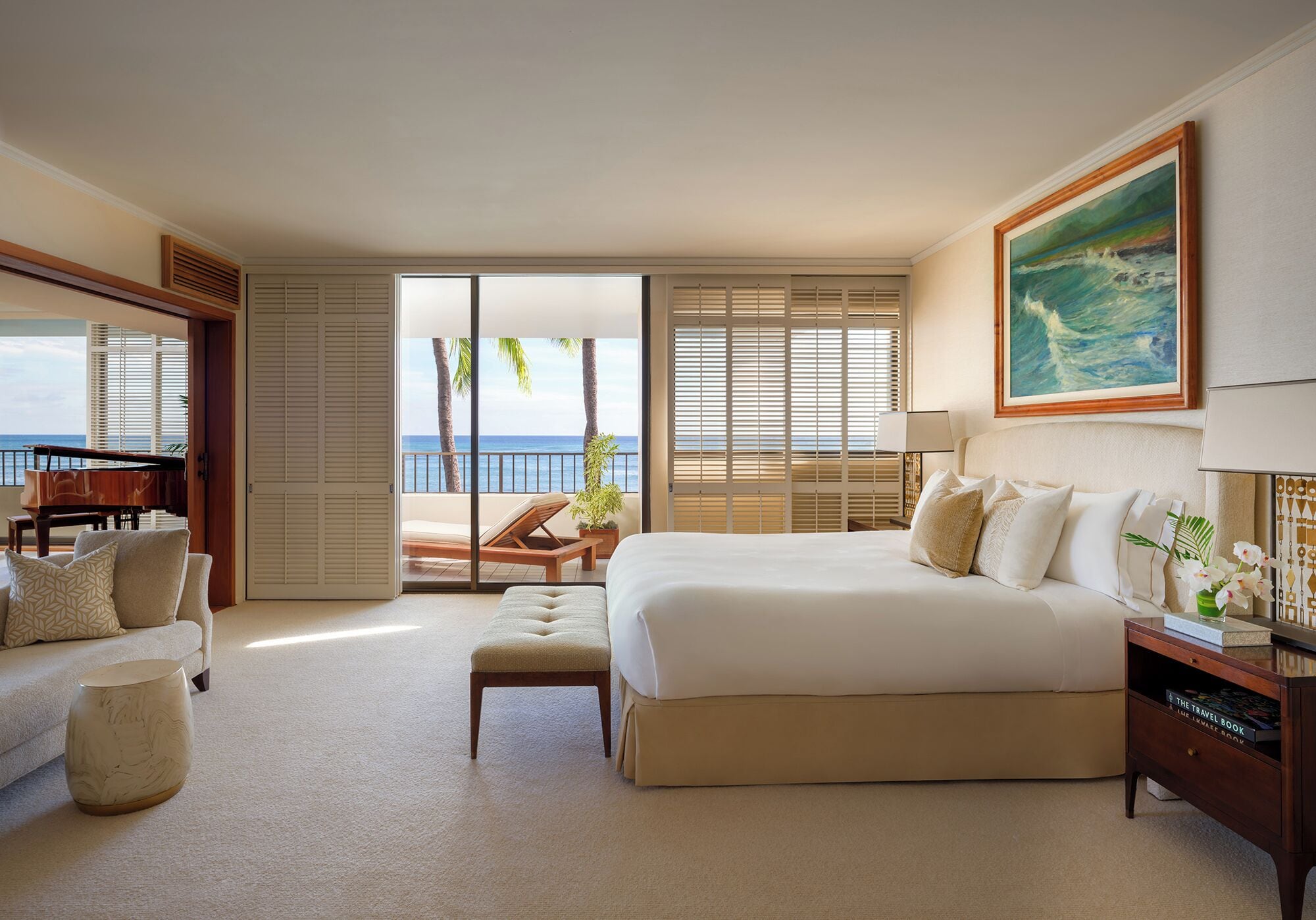 A hotel room with a large bed, a piano, a balcony with a view of the ocean, and a painting on the wall.
