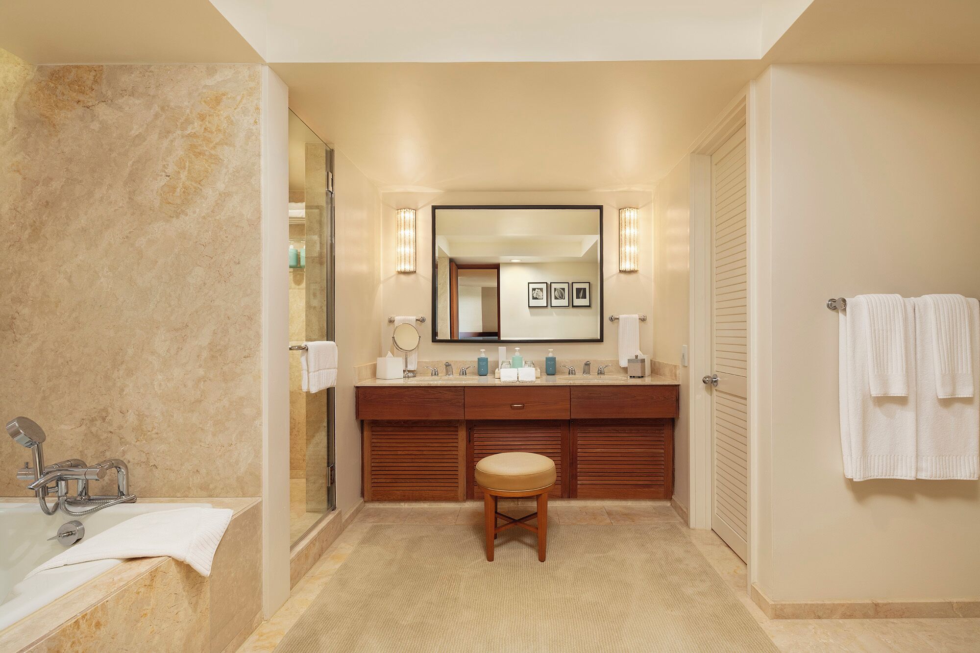 Un baño de hotel con una bañera, un lavabo con espejo, un tocador con un taburete y un perchero para toallas.
