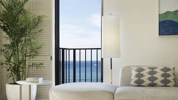 A modern living room with a round coffee table, a sofa, a potted plant, and a view of the ocean through a sliding door.