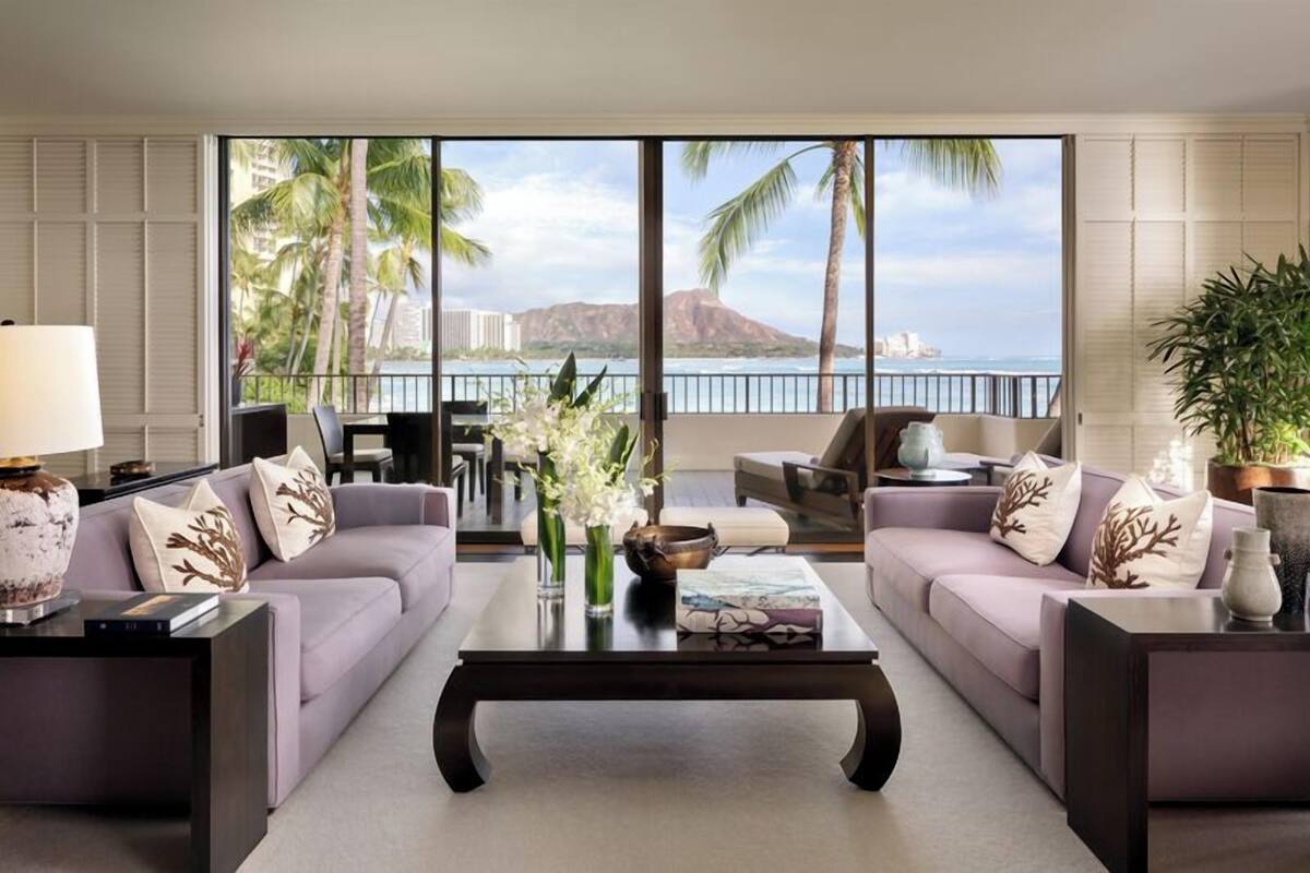 A modern living room with two sofas, a coffee table, and a view of a tropical landscape through large windows.
