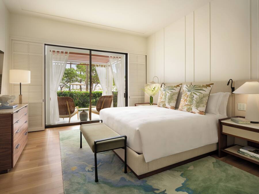 A bedroom with a bed, bedside tables, a bench, a dresser, and a view of the outdoors through a sliding door.