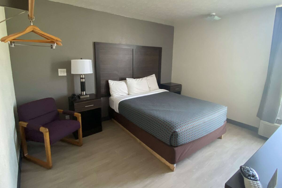 A hotel room with a bed, a chair, a nightstand, and a lamp.