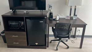 A hotel room with a dark wooden desk, a flat-screen TV, a refrigerator, a microwave, a coffee maker, a chair, and a lamp. - Travelodge by Wyndham Gallipolis (Gallipolis)