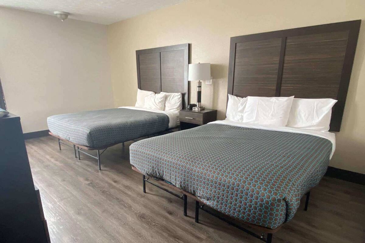 A hotel room with two beds, a nightstand with a lamp, and a desk with a computer.