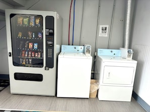 A laundromat with a vending machine, two Whirlpool dryers, and a trash bin.