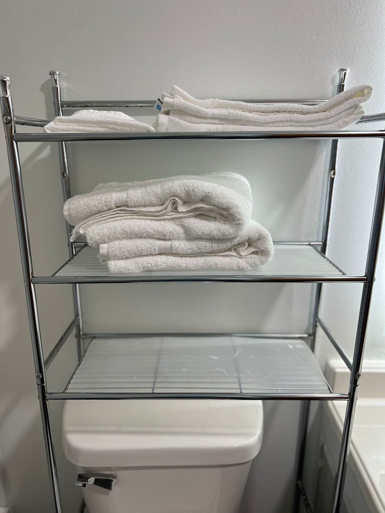 Une étagère métallique à trois niveaux, chaque niveau étant utilisé pour ranger des serviettes blanches pliées.