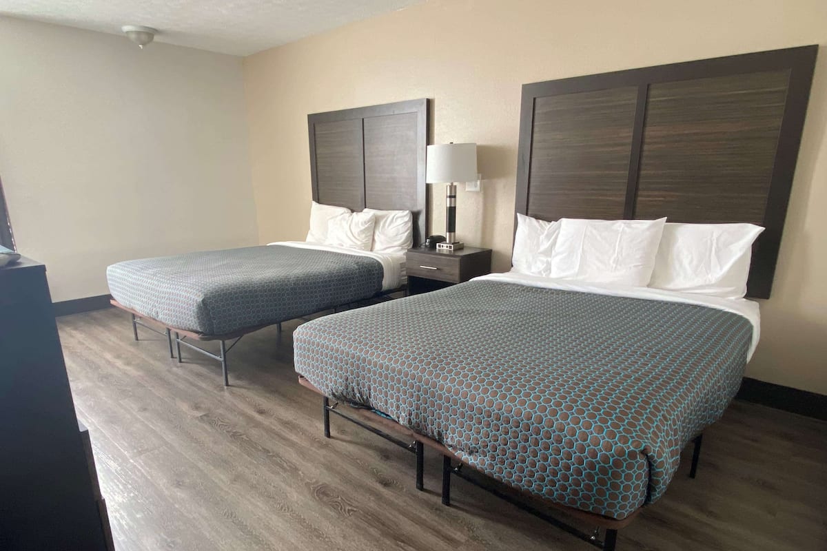 A hotel room with two beds, each with a headboard, a bedside table with a lamp, and a wooden floor.