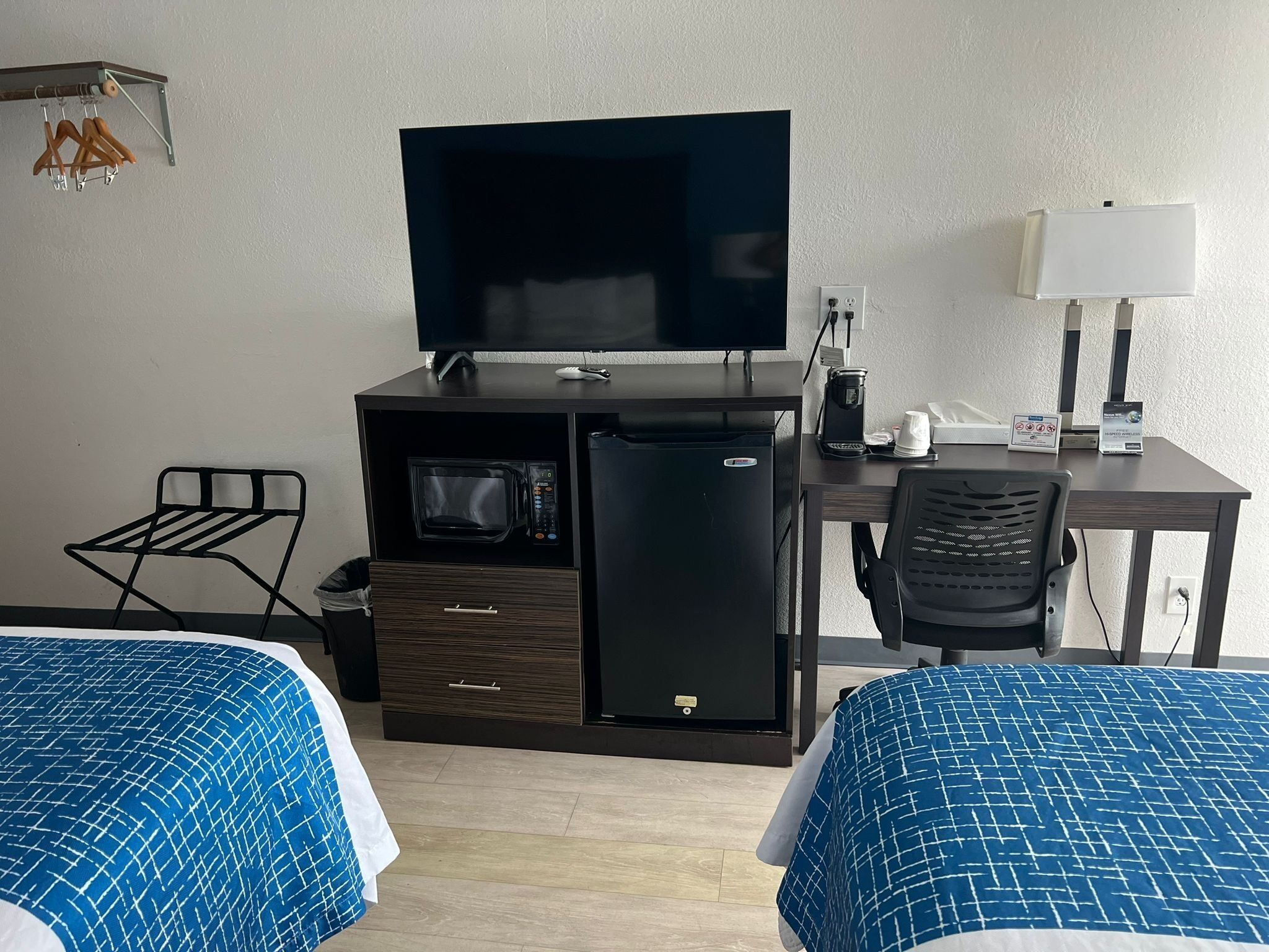 Camera d'albergo con due letti, televisione, frigorifero, microonde, una scrivania con lampada e una sedia.