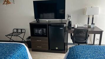Camera d'albergo con due letti, televisione, frigorifero, microonde, una scrivania con lampada e una sedia.