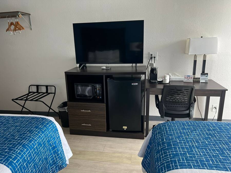 Camera d'albergo con due letti, televisione, frigorifero, microonde, una scrivania con lampada e una sedia.