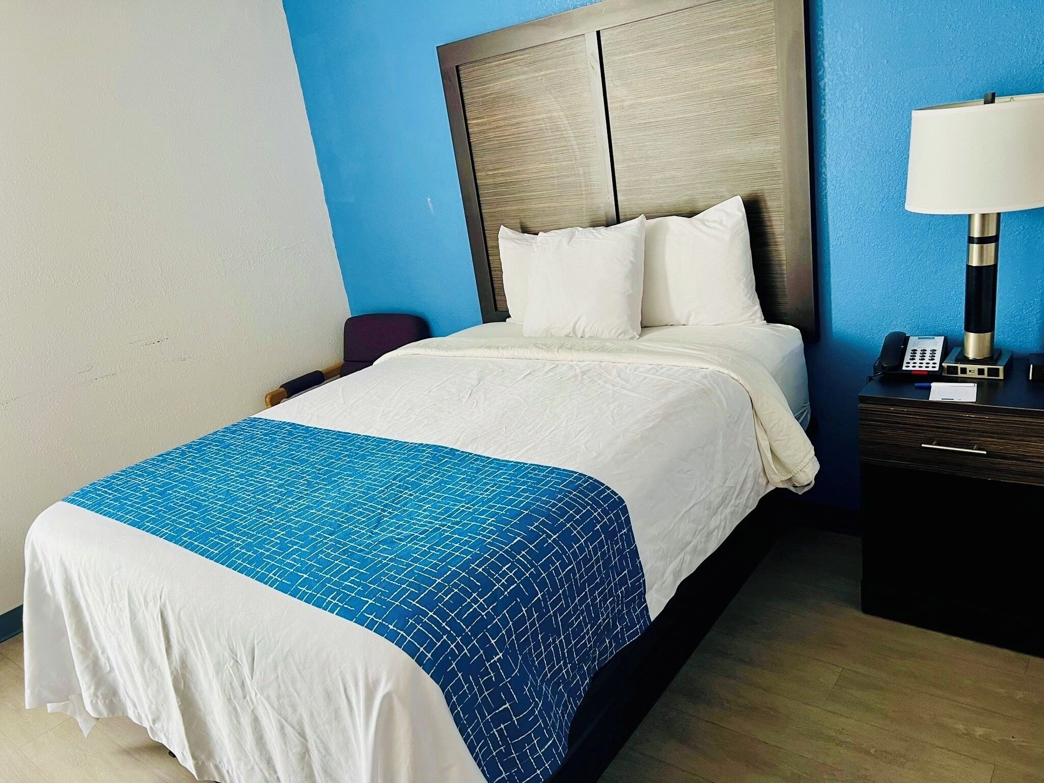 A hotel room with a bed, a nightstand with a lamp, and a phone.