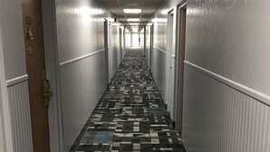 A long, narrow hotel corridor with patterned carpet, white walls, and doors on both sides. - Travelodge by Wyndham Gallipolis (Gallipolis)