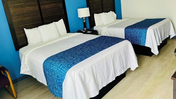 A hotel room with two beds, each with a blue and white bedspread, a wooden headboard, and a nightstand with a lamp. - Travelodge by Wyndham Gallipolis (Gallipolis)