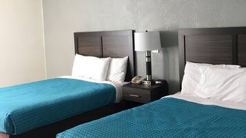 A hotel room with two beds, each with a blue patterned bedspread, a wooden headboard, a bedside table with a lamp, and a telephone.