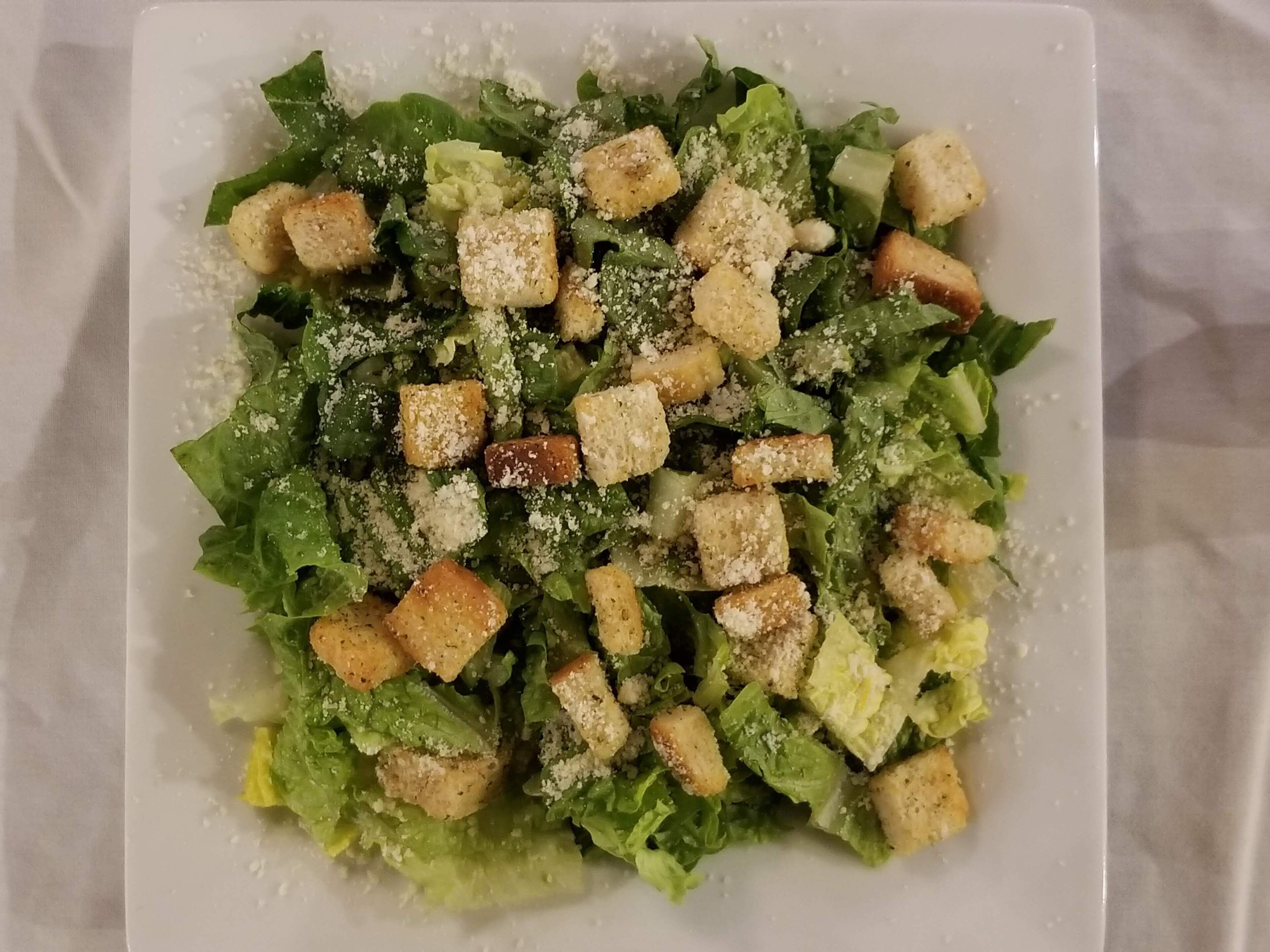 A plate of Caesar salad with croutons and grated cheese.
