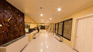 A spacious hotel lobby with a decorative wooden panel, a reception desk, and a large glass door.