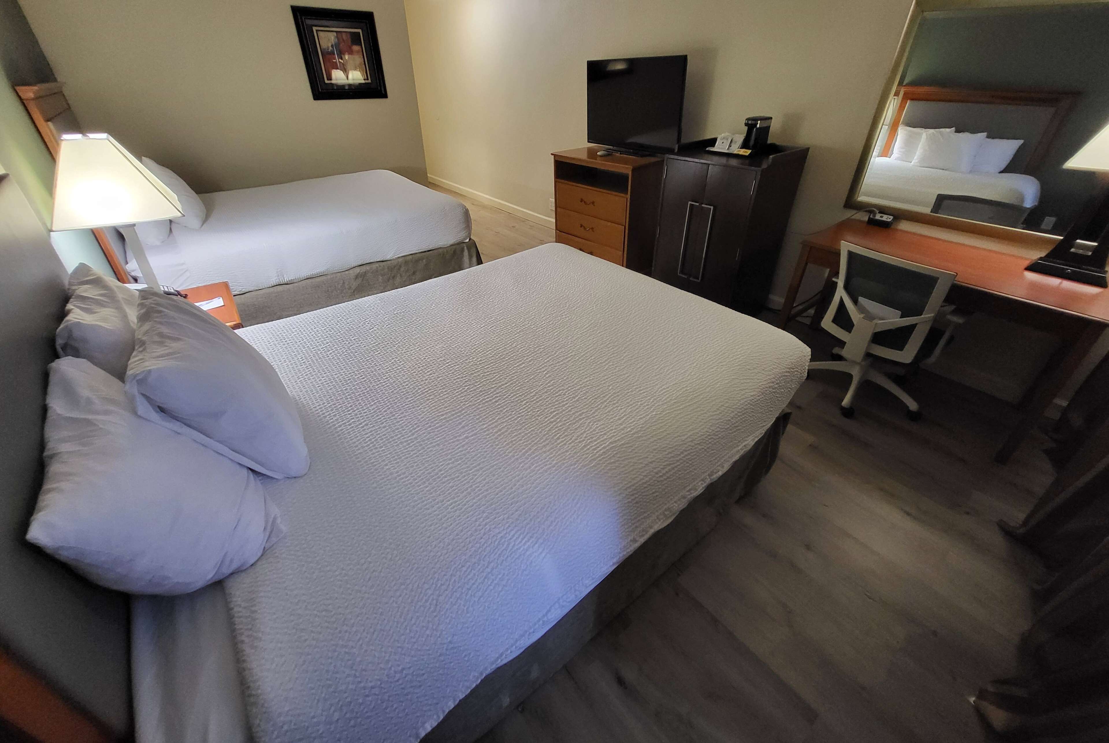 A hotel room with two beds, a desk, a chair, a TV, and a mirror.