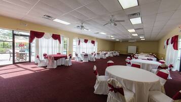 Un salón de banquetes con mesas redondas y sillas, manteles blancos y cintas rojas.