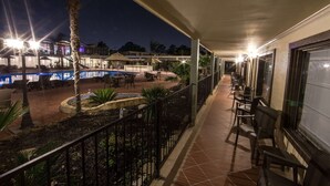 A nighttime view of a hotel balcony with a pool, outdoor seating, and a view of the surrounding buildings.