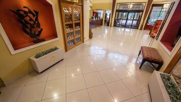 A hotel lobby with a tiled floor, a reception desk, a wine display, and a seating area.