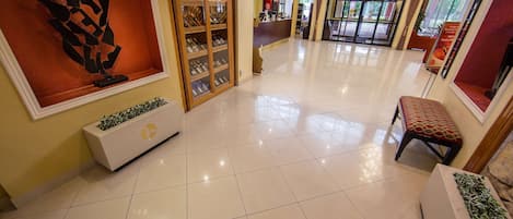 A hotel lobby with a tiled floor, a reception desk, a wine display, and a seating area.