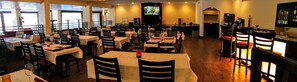 A restaurant with multiple tables and chairs, a bar area, and a television screen. - Ramada by Wyndham Houston Intercontinental Airport East (Humble)