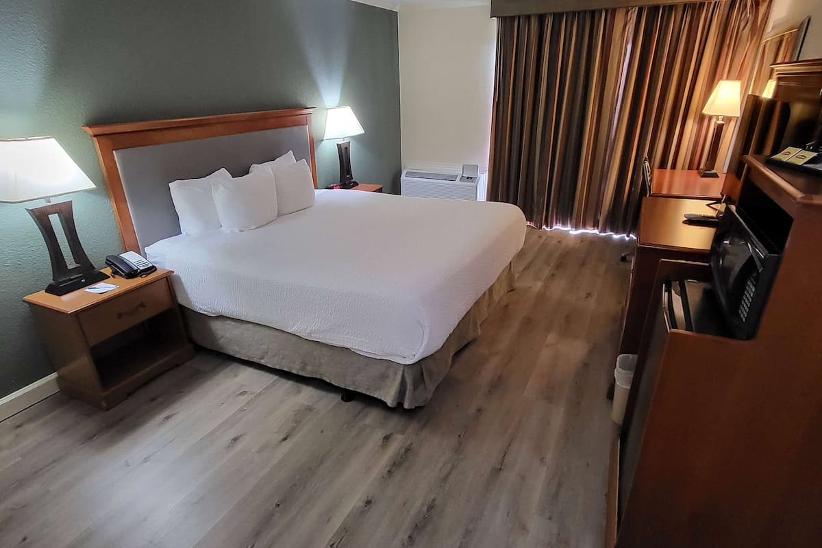 Een hotelkamer met een groot bed, nachtkastjes met lampen, een televisie en een airconditioner.
