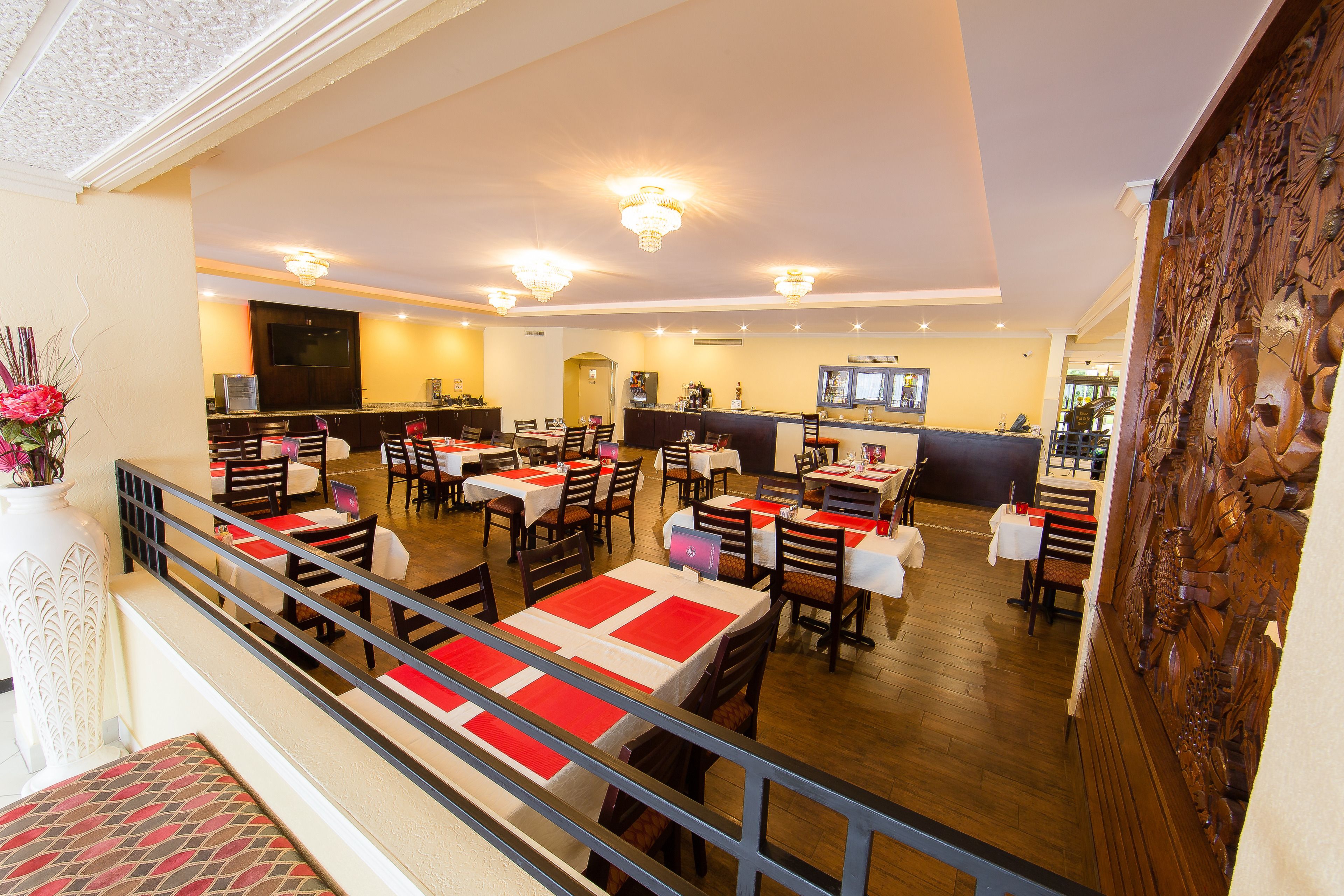 Un ristorante spazioso con numerosi tavoli e sedie, una zona bar e un pannello decorativo in legno sulla destra.