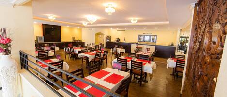 Un ristorante spazioso con numerosi tavoli e sedie, una zona bar e un pannello decorativo in legno sulla destra.