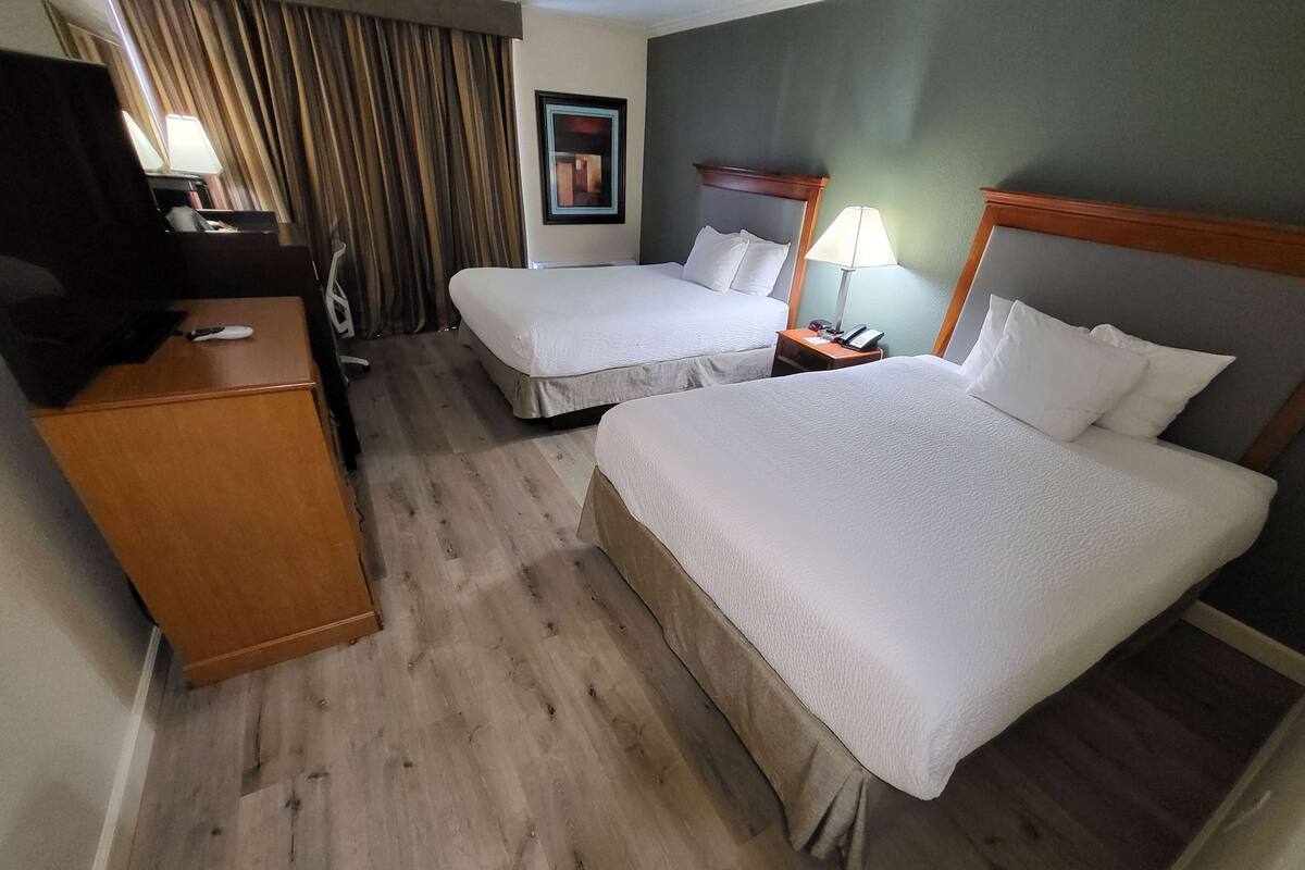 Een hotelkamer met twee bedden, een bureau met een televisie, een lamp en een schilderij aan de muur.