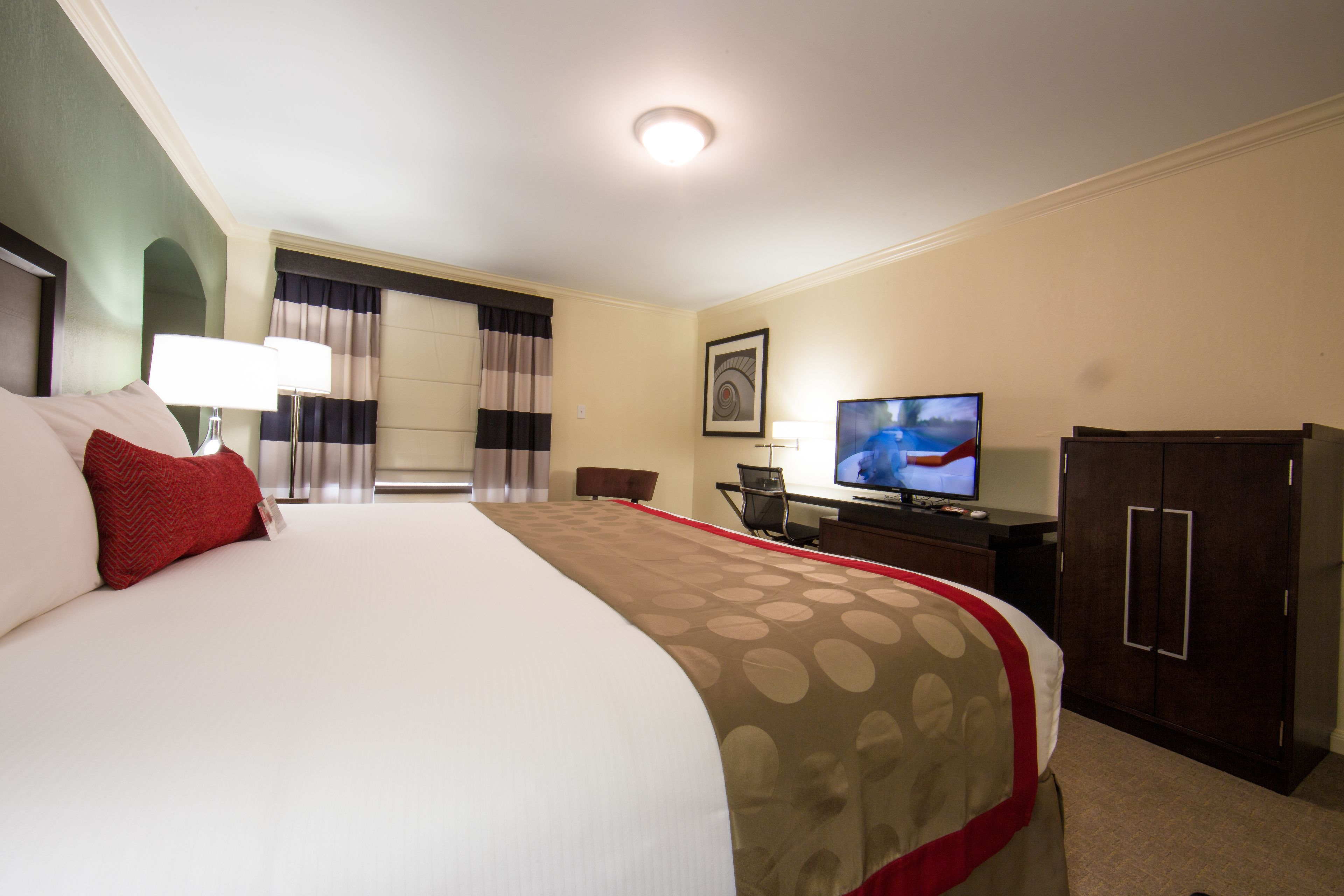 A hotel room with a large bed, a desk with a computer, a television, and a wardrobe.