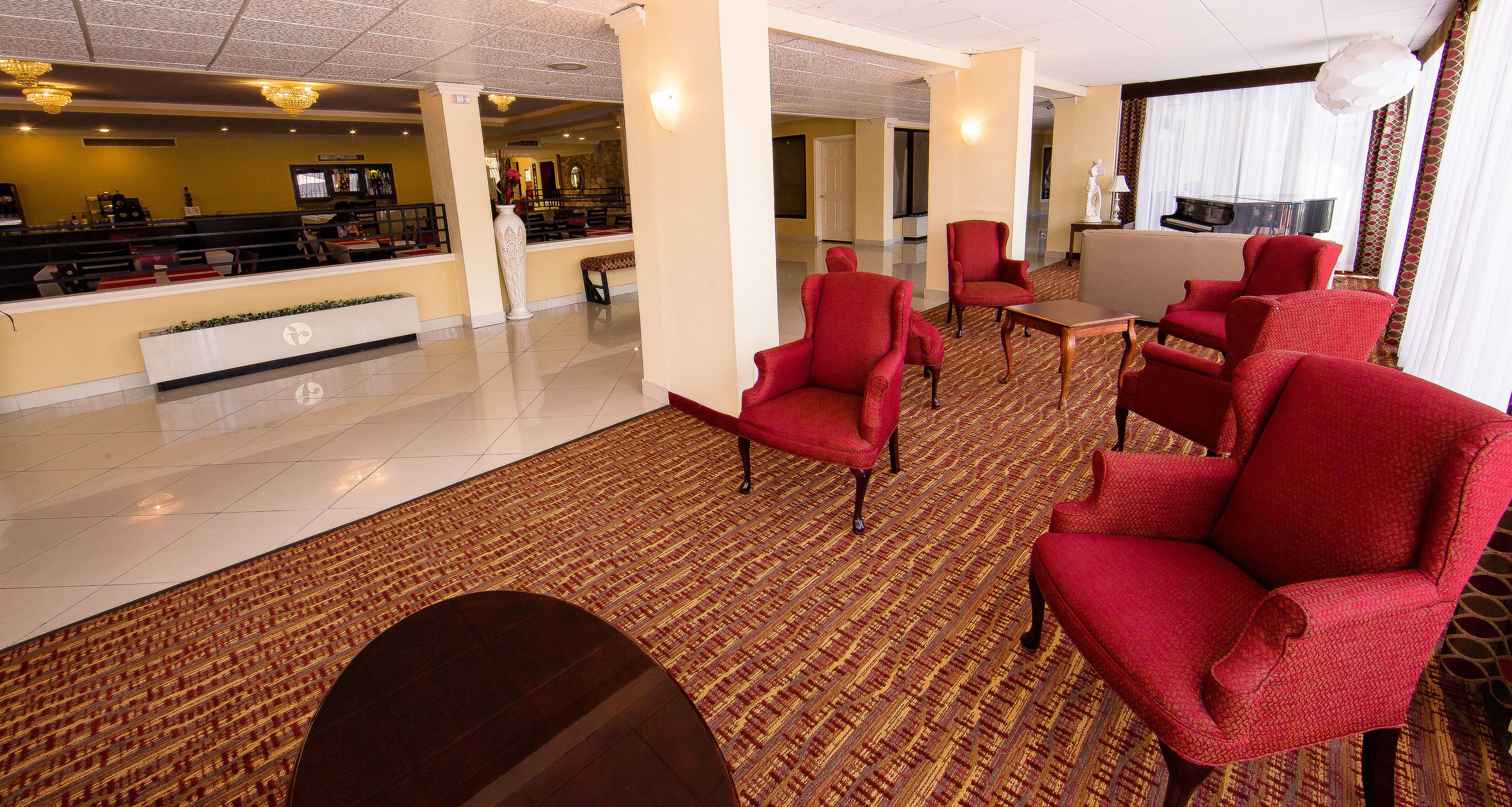 A hotel lobby with a reception desk, red armchairs, a sofa, and a piano.