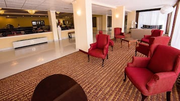 A hotel lobby with a reception desk, red armchairs, a sofa, and a piano.