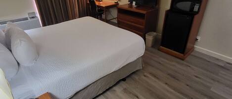 A hotel room with a large bed, a desk with a chair, a television, a microwave, and a telephone.