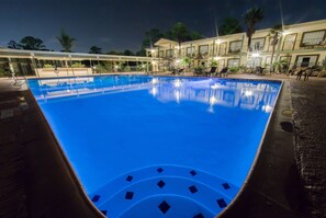 Une piscine à l’eau d’un bleu cristallin, entourée d’un espace abrité avec des sièges, et un bâtiment visible au fond.