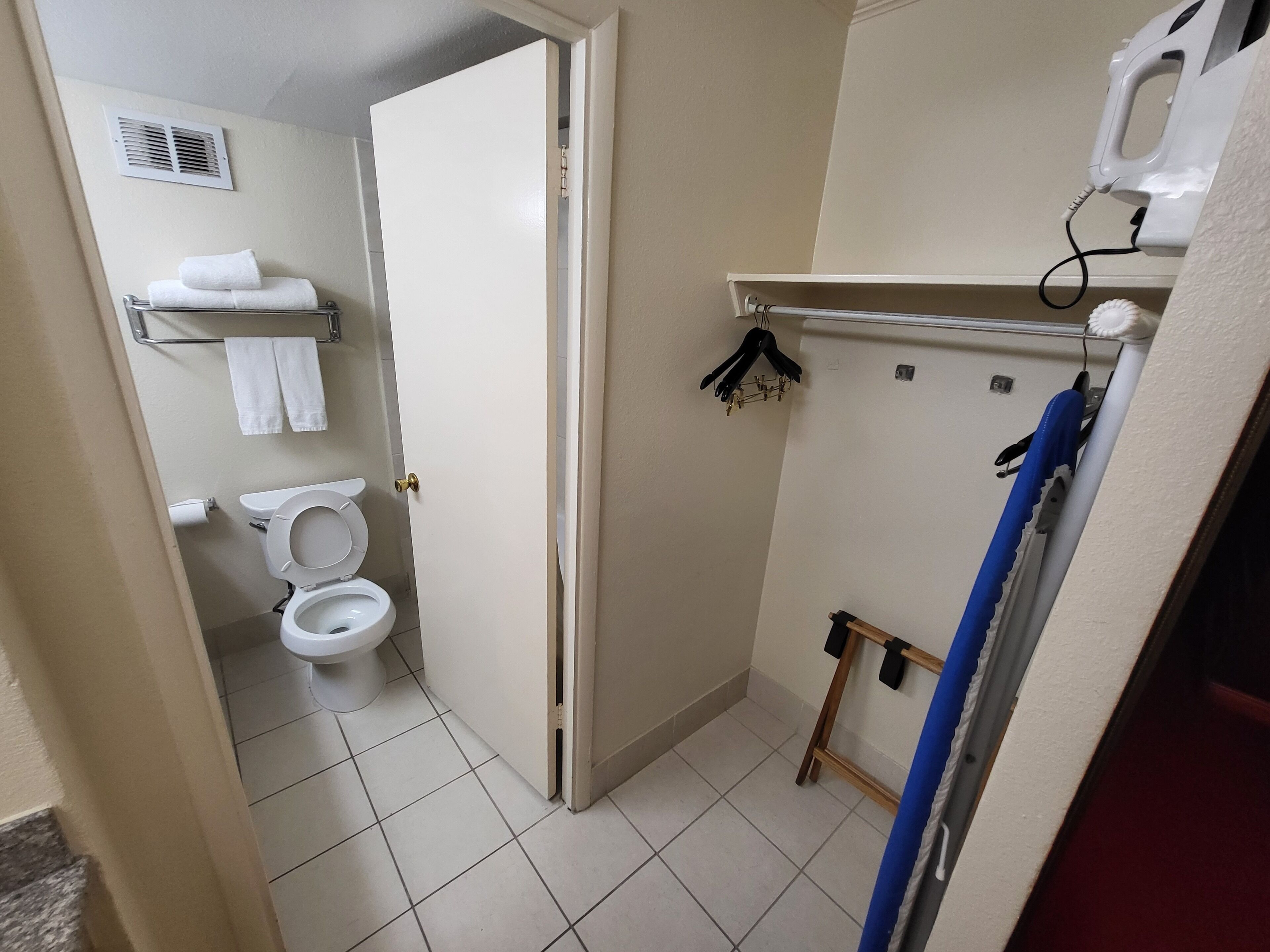 A small bathroom with a toilet, a towel rack with towels, a shower area, and a shelf with a hairdryer.