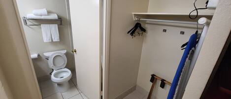 A small bathroom with a toilet, a towel rack with towels, a shower area, and a shelf with a hairdryer.