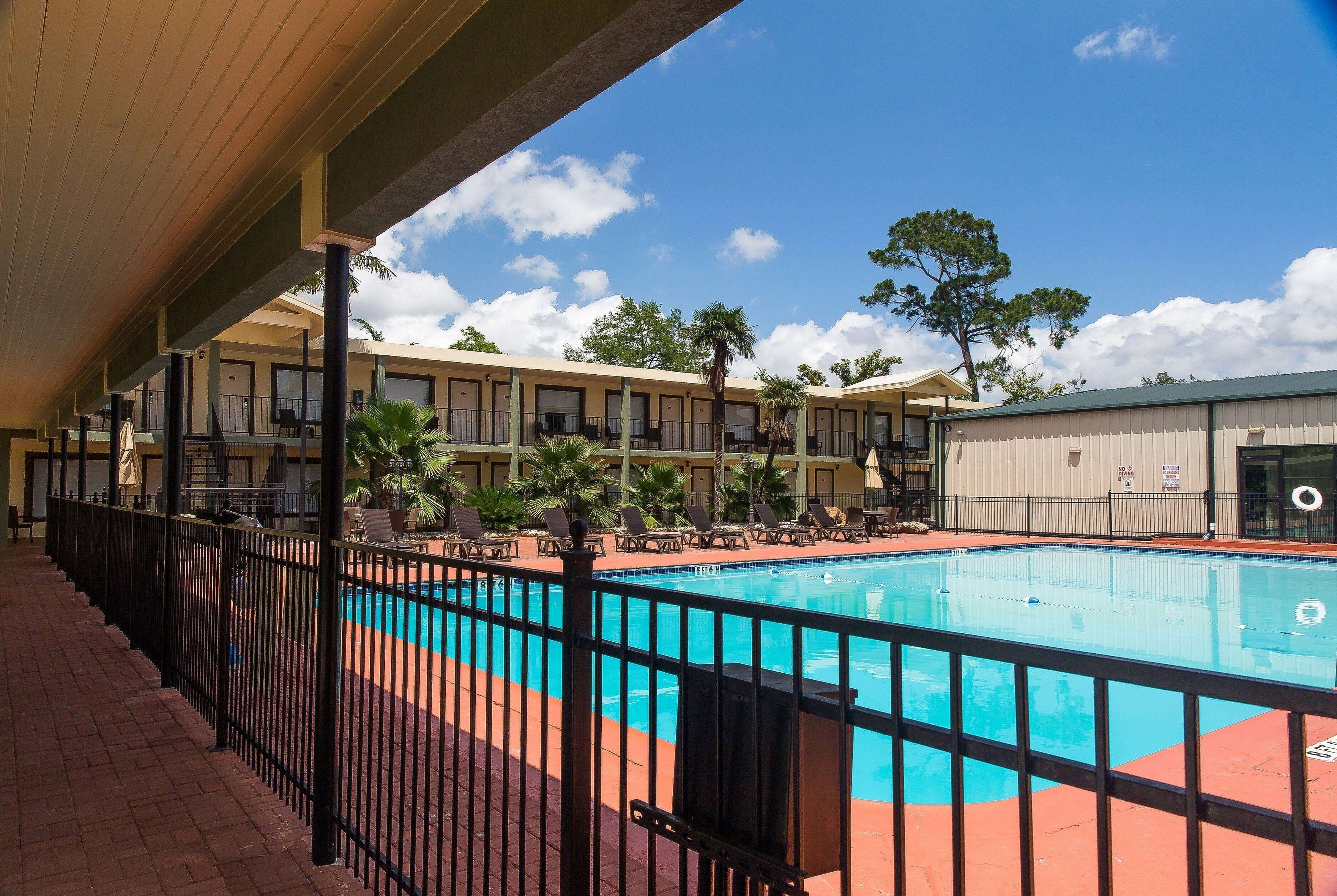 A pool area with a fenced deck, lounge chairs, and a building with multiple balconies in the background.