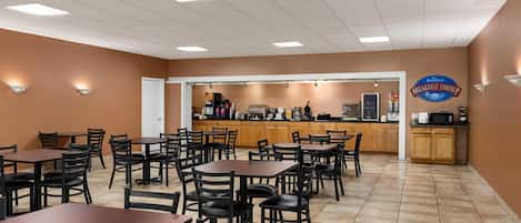 A restaurant with multiple tables and chairs, a kitchen area, and a sign that reads "Baymont Breakfast Corner".