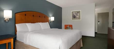 A hotel room with a large bed, two bedside tables, a nightstand, a wall-mounted lamp, a painting, and a door leading to another room.