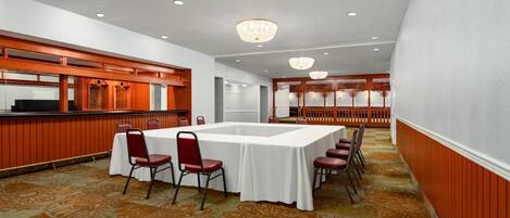 A conference room with a large table, red chairs, and a patterned carpet.
