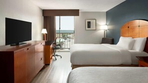 Ein Hotelzimmer mit einem großen Bett, einem Schreibtisch mit Stuhl, einem Fernseher und einem Fenster mit Vorhängen.