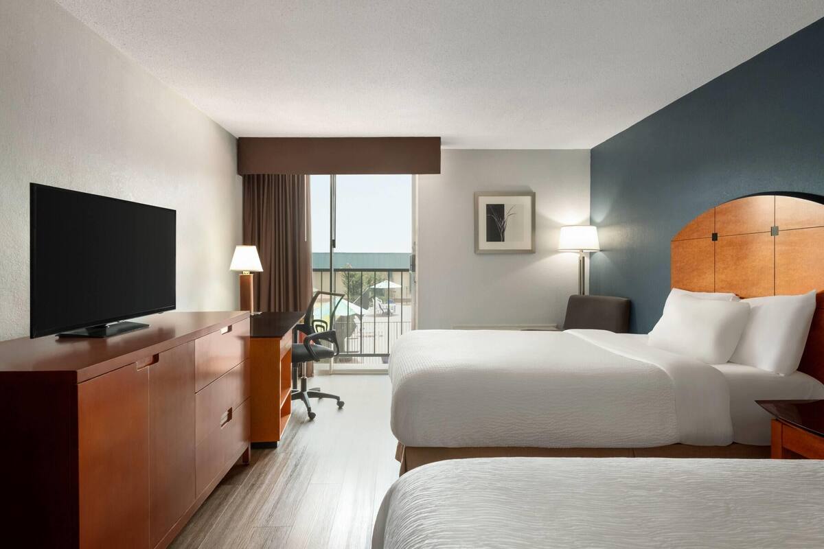 Una habitación de hotel con una cama grande, un escritorio con silla, televisión y ventana con cortinas.