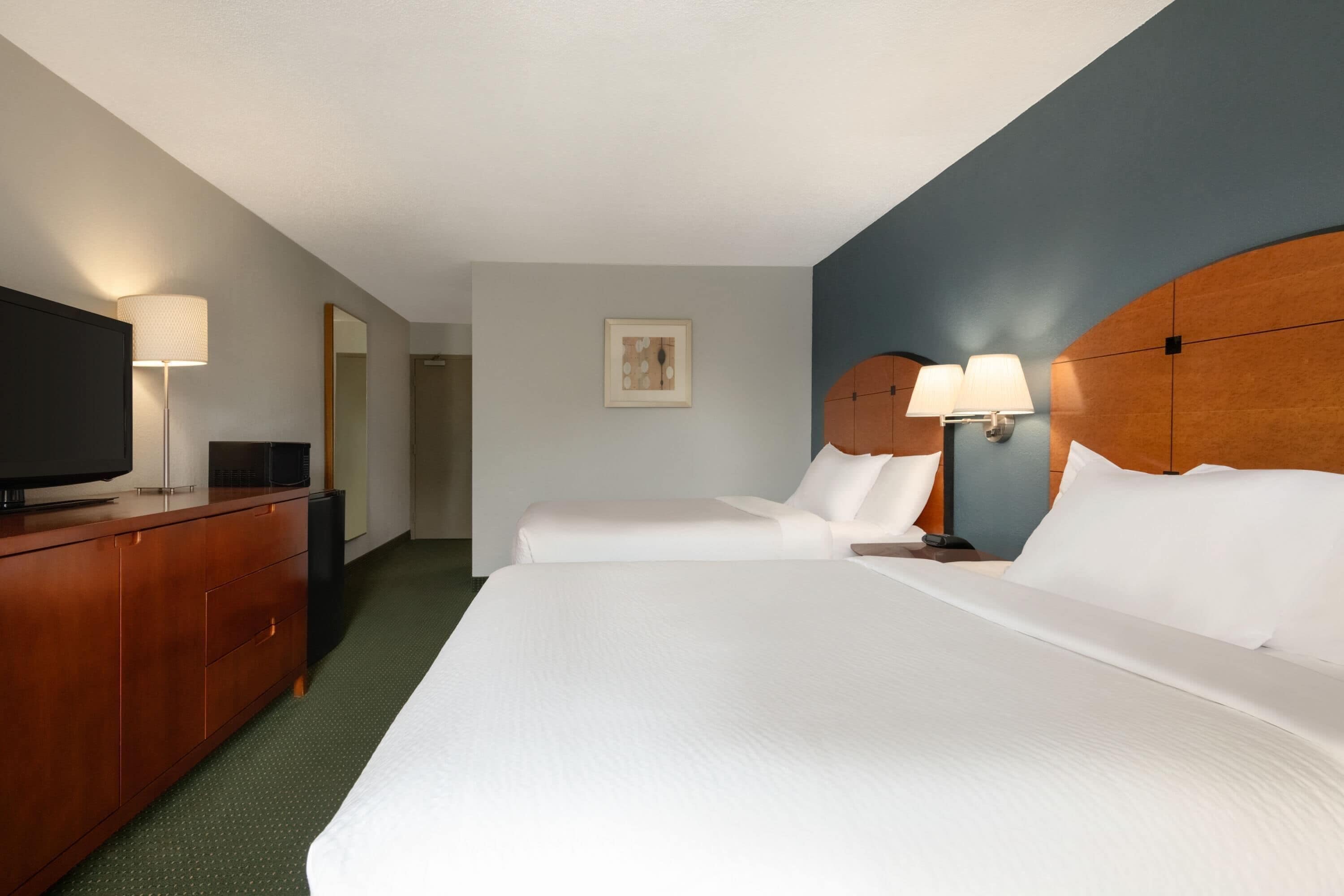 A hotel room with two beds, a wooden dresser, a flat-screen TV, and a framed picture on the wall.