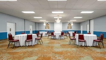 Una sala de conferencias con varias mesas redondas, sillas rojas y una alfombra estampada.